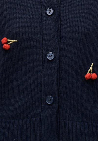 Σκούρα ναυτική πλεκτή ζακέτα με τέσσερα κουμπιά και μικρά κόκκινα πλεκτά σχέδια κερασιών στα αριστερά και δεξιά κοντά στο στήθος.