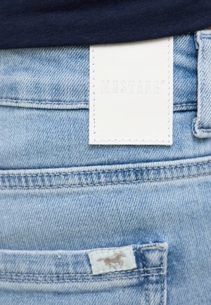 Lichtblauwe denim jeans met een witte leren merklabel. Heeft een achterzak met stikseldetails en een klein logo-label.
