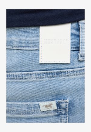 Heledad sinine teksapüksid valge nahast brändi sildiga. Omad tagatasku koos õmblusdetailidega ja väikese logo sildiga.