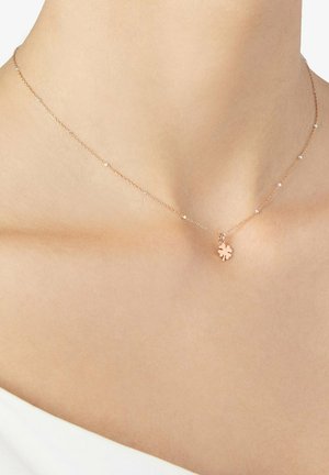 Delikate goldene Halskette mit kleinen, gleichmäßig verteilten Perlen und einem vierblättrigen Kleeblatt-Anhänger, der in der Mitte des Halses ruht.