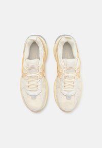 Zapatillas deportivas de malla en crema y beige con sutiles acentos plateados, que cuentan con una suela gruesa y múltiples lazos para cordones que permiten un ajuste ajustable.