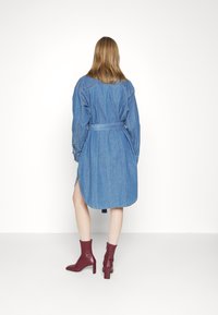 Denim shirt dress with long sleeves, belted waist, rounded hem, side slits, in light blue; paired with burgundy ankle boots.