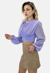 Lawendowa krótka bluzka z bufkami na rękawach i marszczonym paskiem w talii, zestawiona z beżową mini spódnicą zamszową. Dopełniona bransoletką na nadgarstku.
