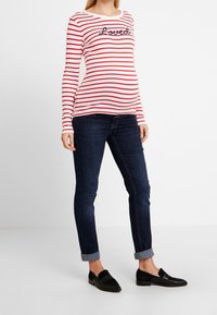 Röd och vit randig långärmad tröja med texten "Loved"; ihop med mörka jeans och svarta skor, med uppvikta ärmar.