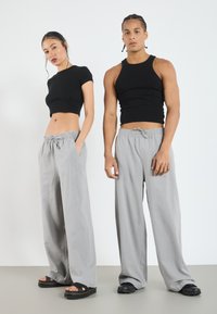 Des crop tops ajustés noirs associés à un pantalon gris ample avec une taille élastique, tous deux en tissu doux. Des sandales noires complètent le look.