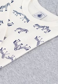 Weißes Hemd mit navyfarbenem Zebra-Muster, über einem hellgrauen Shirt in Schichten getragen, beide mit Rundhalsausschnitten und aus weichem Baumwollstoff.