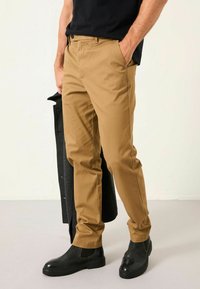 Helle Tan-Chinos aus leichtem Stoff, mit geradem Bein, standardmäßigen Taschen und kombiniert mit schwarzen Knöchelstiefeln.