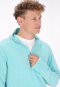 Lichtblauwe fleece half-rits pullover met lange mouwen, zachte textuur en een staande kraag. Voorzien van een ritssluiting aan de voorkant.