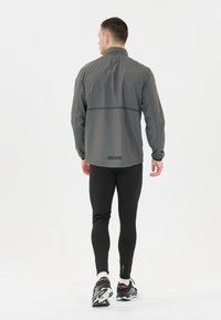 Leichte graue Laufjacke für Herren mit hohem Kragen, langen Ärmeln, elastischen Bündchen und einem reflektierenden Band über den Rücken.