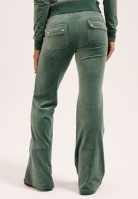 Grüne, weich gemusterte Flared-Hosen aus Cord mit Rückentaschen und Druckknopfverschlüssen, sanfter Textur und tailliertem Schnitt.