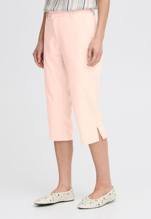 Pale pink cropped pants with side slits, made of smooth fabric. Worn with a striped top and light-colored, studded flats.