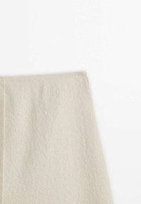 Knälång, off-white kjol i texturerad tyg med en slät yta och en dold dragkedja i ryggen för stängning.