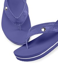 Violet flip-flopit, där texturerade remmar är prydda med vita prickar och en metallisk detalj. Tjock sula med vit randdetalj.
