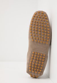 Suede shoe sole in light brown with raised, round rubber studs in orange. Textured surface is designed for grip and traction.