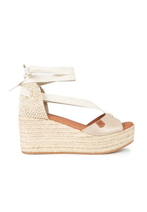Sandalias cuña en beige, con un upper brillante, suela de yute trenzado y cintas en el tobillo. Textura suave y detalle sutil del logo en la parte delantera.