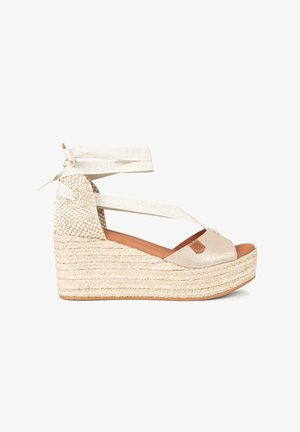 Sandalias cuña en beige, con un upper brillante, suela de yute trenzado y cintas en el tobillo. Textura suave y detalle sutil del logo en la parte delantera.