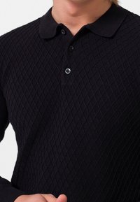 Polo-shirt tricoté noir avec un motif en losanges, un col classique et une patte de boutonnage à trois boutons avec des boutons noirs.