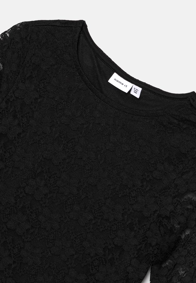 Top en dentelle noire avec un col rond et un motif floral texturé, avec une doublure intérieure lisse et une étiquette de la marque sur le col.