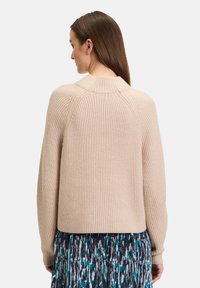 Beiger Strickpullover mit gerippter Textur, Raglanärmeln und abgerundetem Saum, kombiniert mit einem plissierten Rock in Blau- und Grüntönen.