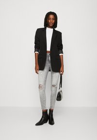Blazer negro, top corto blanco, jeans ajustados gris rasgados, botas negras hasta el tobillo y bolso pequeño negro. Tejido suave con diseño estructurado.