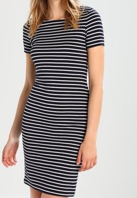 Robe ajustée à rayures bleu marine et blanches, avec des manches courtes, un col rond et une texture douce, arrivant au-dessus du genou.