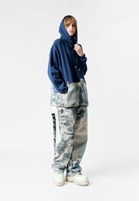 Sudadera azul marino con una sección inferior de mezclilla a rayas en azul y gris, combinada con pantalones sueltos de patrón similar y botas gruesas blancas.