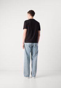 Tricou negru din bumbac, cu mâneci scurte, asociat cu blugi deschiși la culoare, de tip relaxat. Ținuta include adidași albi fără logo-uri vizibile.