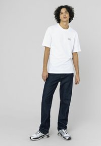 T-shirt en coton blanc à manches courtes et col rond, associé à un jean en denim bleu foncé et des chaussures de sport argentées.