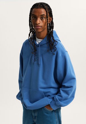 Blue hoodie made of soft fabric with a kangaroo pocket and ribbed cuffs. Features a tonal logo on the front and loose fit design.