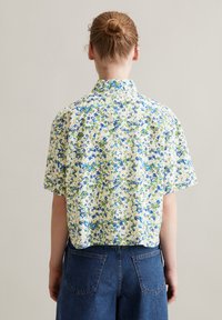 Kurzarmhemd mit einem floralen Muster in Blau und Grün auf einem cremefarbenen Hintergrund, mit einem spitzen Kragen und entspannter Passform.