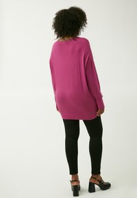 Magenta-oversized Pullover mit langen Ärmeln und geripptem Saum, kombiniert mit schwarzen Leggings und klobigen Blockabsatzsandalen. Strukturierter, lässiger Look.
