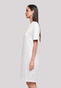 Weißes Baumwoll-T-Shirt-Kleid mit lässiger Passform, kurzen Ärmeln und einem gelben Grafikdruck auf der Vorderseite. Verfügt über einen grünen Akzent am Saum.