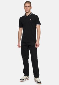 Zwart polo shirt met contrasterende ribgebreide kraag en mouwen. Gekomplementeerd met zwarte jeans en meerkleurige sneakers, met een logo op de borst.