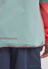 Helles blaues Jacket mit einem korallenfarbenen Akzent am Saum. Hat eine glatte Textur, einen silbernen reflektierenden Streifen und einen elastischen Abschluß.