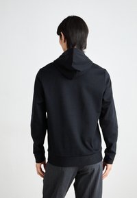 Hoodie noir à rayures avec une texture douce, doté d'une capuche, de poignets côtelés et d'une taille ajustée, associé à un pantalon gris à rayures.