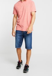Red heather knit t-shirt, blue denim shorts, and black athletic shoes with colorful accents, standing on a light background.