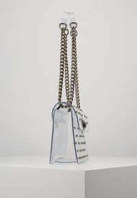 Borsa trasparente in acrilico con borchie in metallo argentato e tracolle a catena. Presenta una forma strutturata e una chiusura a pattina con un accento metallico.