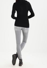 Sort striktruet sweater med bred krave, kombineret med tætsiddende grå jeans og sorte ankelstøvler med lynlås. Rent, minimalistisk design.