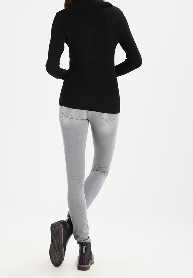 Sort striktruet sweater med bred krave, kombineret med tætsiddende grå jeans og sorte ankelstøvler med lynlås. Rent, minimalistisk design.