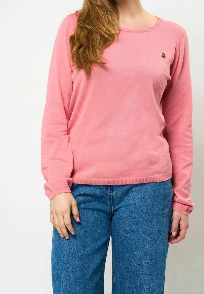 Maglione rosa a maniche lunghe con scollatura a girocollo e piccolo dettaglio ricamato. Abbinato a jeans in denim blu a gamba larga. Tessuto morbido.