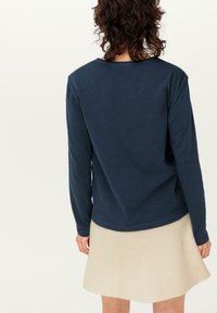 Navyblaues Langarmshirt mit Rundhalsausschnitt, weichem Baumwollmaterial und lässiger Passform, kombiniert mit einem gerippten cremfarbenen Rock.