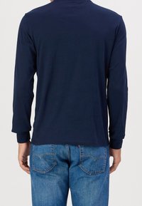 Navyblaues Langarmshirt aus Baumwolle, mit Rundhalsausschnitt und eng anliegenden Bündchen, kombiniert mit blauen Jeans im klassischen Taschenformat.