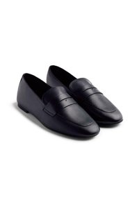 Mocasines de cuero negro con una textura suave, punta redondeada y detalles de costura en la parte superior, presentan un perfil bajo y suela plana.