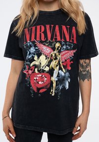 Black oversized t-shirt featuring a multicolored graphic of a skeletal figure with wings, adorned with floral patterns and the word "NIRVANA."