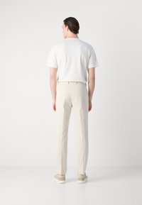 Herenoutfit met een wit T-shirt met korte mouwen, lichtbeige gestructureerde broek en beige sneakers met een contrasterende zool.