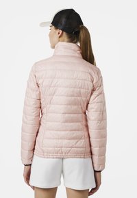 Ljust rosa pufferjacka med vertikalt kviltat mönster, hög krage och elastisk nederkant. Bärs med vita shorts och en svart nätbasballkeps.