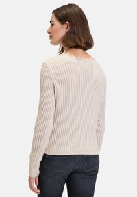 Hellbeige gestrickter Pullover mit einem gerippten Muster, weitem Ausschnitt und langen Ärmeln, kombiniert mit dunklen Jeans.