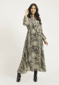 Robe longue et fluide en noir et crème avec des motifs complexes. Dotée de manches longues, d'un col boutonné et d'une taille cintrée. Portée avec des bottes noires.