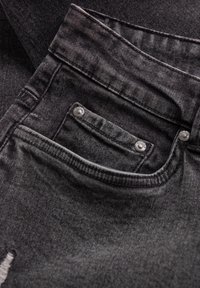 Gros plan sur la poche avant d'un jean en denim gris foncé avec des rivets métalliques et des détails de couture visibles.