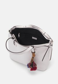 Jasnoróżowa skórzana torebka na jeden pasek, z otwartym zamkiem błyskawicznym u góry, czarnym wnętrzem oraz kolorowym frędzlem przywieszonym do ringa uchwytu.